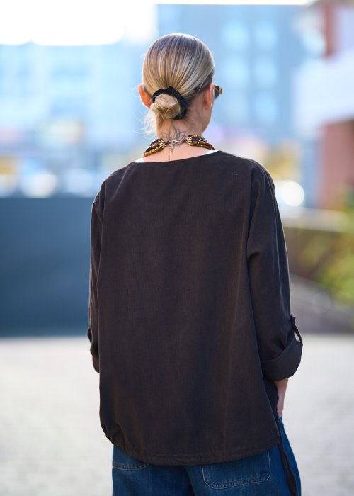 Bluzka oversize w kolorze głębokiego brązu z długim rękawem i regulowanym dołem na troczki, zestawiona z jeansami w miejskiej stylizacji