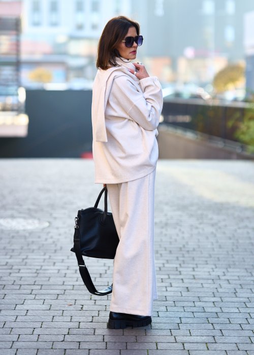 Kobieta w jasnym beżowym dresowym komplecie z szerokim golfem zapinanym na guziki