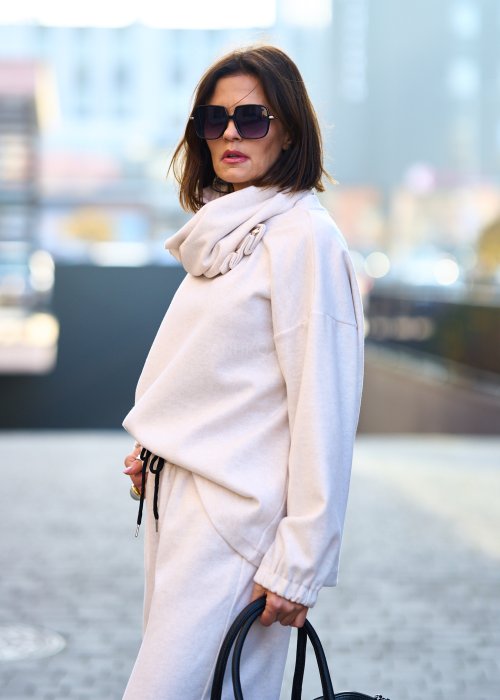 Kobieta w jasnym beżowym dresowym komplecie z szerokim golfem zapinanym na guziki