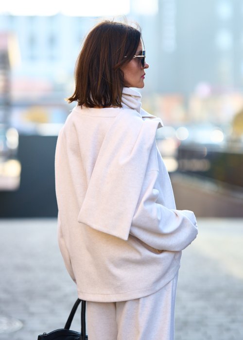 Kobieta w jasnym beżowym dresowym komplecie z szerokim golfem zapinanym na guziki