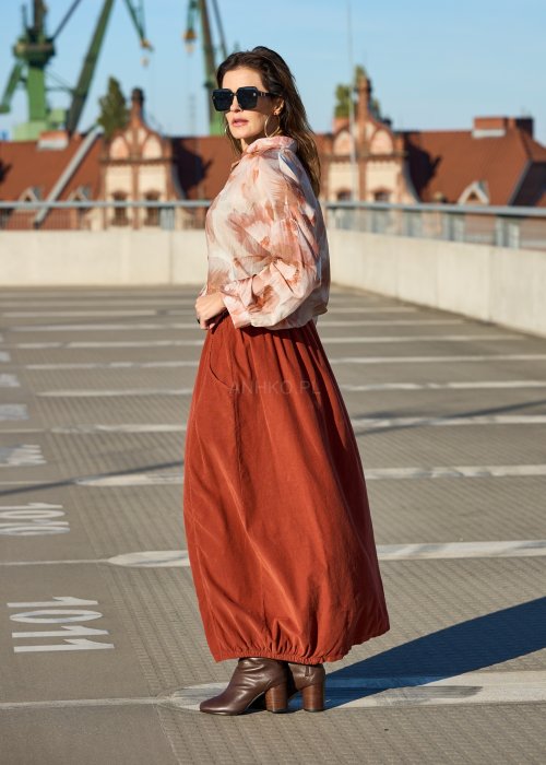 Ceglana spódnica maxi z elastyczną talią i kieszeniami, o luźnym kroju, zestawiona z brązową marynarką i skórzanymi botkami na obcasie w eleganckiej, miejskiej stylizacji.