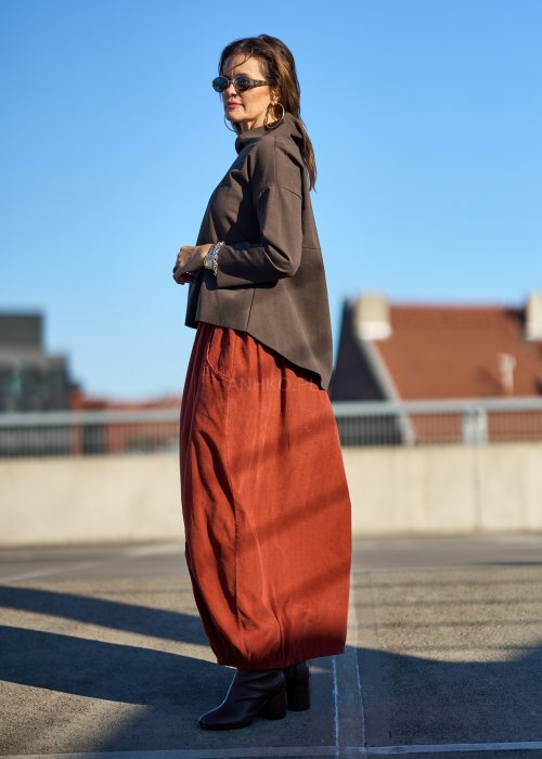 Ceglana spódnica maxi z elastyczną talią i kieszeniami, o luźnym kroju, zestawiona z brązową marynarką i skórzanymi botkami na obcasie w eleganckiej, miejskiej stylizacji.