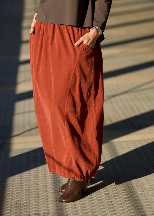 Ceglana spódnica maxi z elastyczną talią i kieszeniami, o luźnym kroju, zestawiona z brązową marynarką i skórzanymi botkami na obcasie w eleganckiej, miejskiej stylizacji.