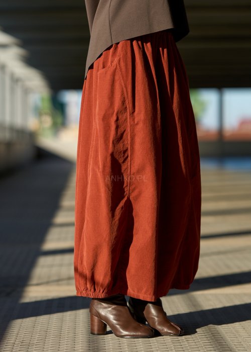 Ceglana spódnica maxi z elastyczną talią i kieszeniami, o luźnym kroju, zestawiona z brązową marynarką i skórzanymi botkami na obcasie w eleganckiej, miejskiej stylizacji.