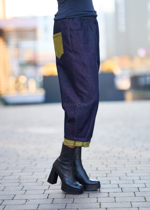 Luźne granatowe spodnie jeansowe z zielonymi detalami na kieszeni i podwiniętych nogawkach, stylizowane z dopasowaną bluzką i botkami na obcasie w miejskim looku.