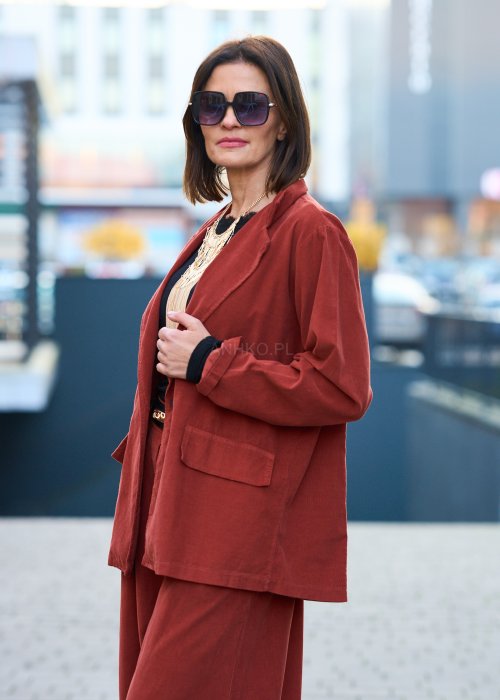 Kobiecy komplet w kolorze ceglastym – luźna marynarka na jeden guzik z naszywanymi kieszeniami oraz szerokie spodnie z wysokim stanem, stylizacja miejska, elegancka i nowoczesna.
