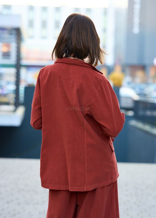 Kobiecy komplet w kolorze ceglastym – luźna marynarka na jeden guzik z naszywanymi kieszeniami oraz szerokie spodnie z wysokim stanem, stylizacja miejska, elegancka i nowoczesna.