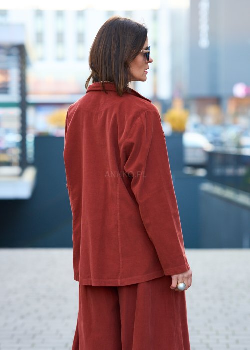Kobiecy komplet w kolorze ceglastym – luźna marynarka na jeden guzik z naszywanymi kieszeniami oraz szerokie spodnie z wysokim stanem, stylizacja miejska, elegancka i nowoczesna.
