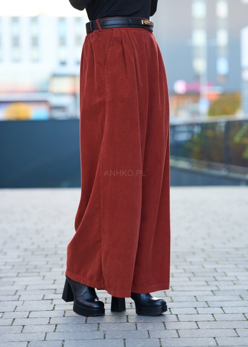 Kobiecy komplet w kolorze ceglastym – luźna marynarka na jeden guzik z naszywanymi kieszeniami oraz szerokie spodnie z wysokim stanem, stylizacja miejska, elegancka i nowoczesna.