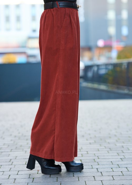 Kobiecy komplet w kolorze ceglastym – luźna marynarka na jeden guzik z naszywanymi kieszeniami oraz szerokie spodnie z wysokim stanem, stylizacja miejska, elegancka i nowoczesna.