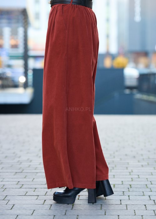 Kobiecy komplet w kolorze ceglastym – luźna marynarka na jeden guzik z naszywanymi kieszeniami oraz szerokie spodnie z wysokim stanem, stylizacja miejska, elegancka i nowoczesna.