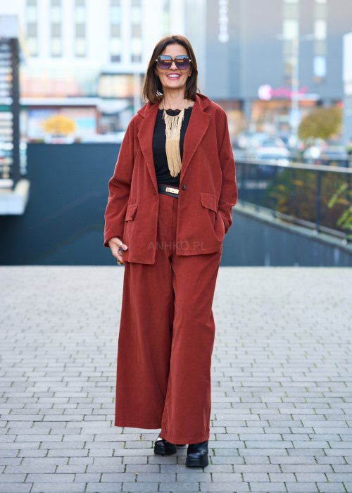 Kobiecy komplet w kolorze ceglastym – luźna marynarka na jeden guzik z naszywanymi kieszeniami oraz szerokie spodnie z wysokim stanem, stylizacja miejska, elegancka i nowoczesna.