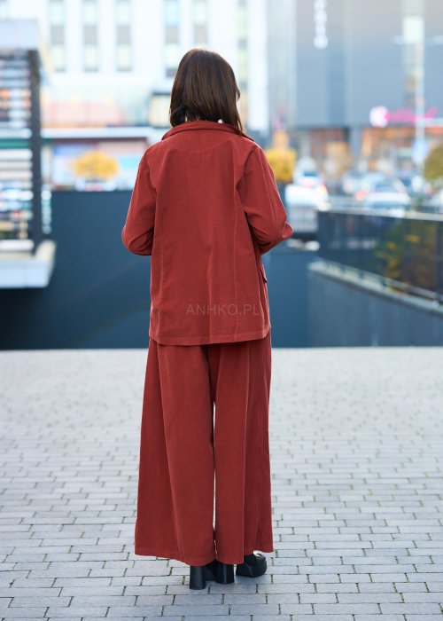Kobiecy komplet w kolorze ceglastym – luźna marynarka na jeden guzik z naszywanymi kieszeniami oraz szerokie spodnie z wysokim stanem, stylizacja miejska, elegancka i nowoczesna.