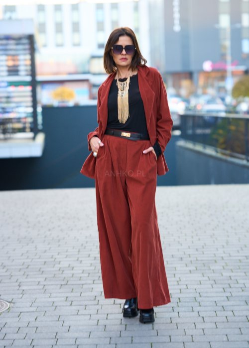 Kobiecy komplet w kolorze ceglastym – luźna marynarka na jeden guzik z naszywanymi kieszeniami oraz szerokie spodnie z wysokim stanem, stylizacja miejska, elegancka i nowoczesna.