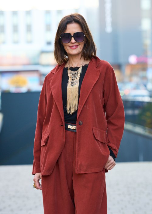 Kobiecy komplet w kolorze ceglastym – luźna marynarka na jeden guzik z naszywanymi kieszeniami oraz szerokie spodnie z wysokim stanem, stylizacja miejska, elegancka i nowoczesna.