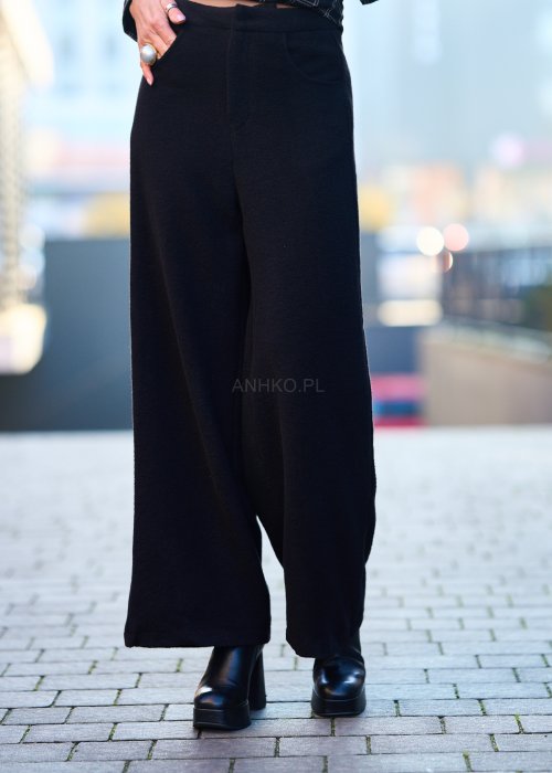 Czarne damskie spodnie z prostą, lekko rozszerzaną nogawką, gładkie, o klasycznym kroju, zestawione z czarnymi botkami na obcasie