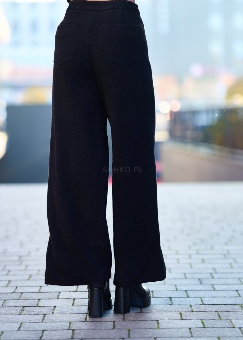 Czarne damskie spodnie z prostą, lekko rozszerzaną nogawką, gładkie, o klasycznym kroju, zestawione z czarnymi botkami na obcasie