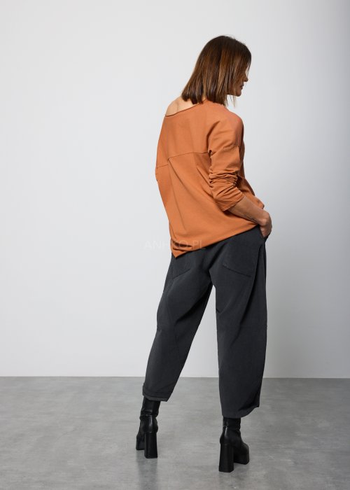 Modelka w brązowej bluzie z długim rękawem i ozdobnym nadrukiem w odcieniach złota i czerni