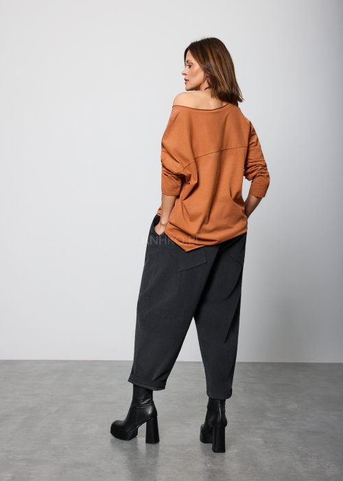 Modelka w brązowej bluzie z długim rękawem i ozdobnym nadrukiem w odcieniach złota i czerni