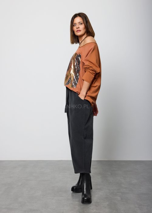 Modelka w brązowej bluzie z długim rękawem i ozdobnym nadrukiem w odcieniach złota i czerni