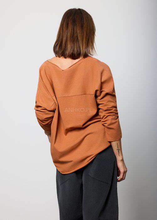 Modelka w brązowej bluzie z długim rękawem i ozdobnym nadrukiem w odcieniach złota i czerni