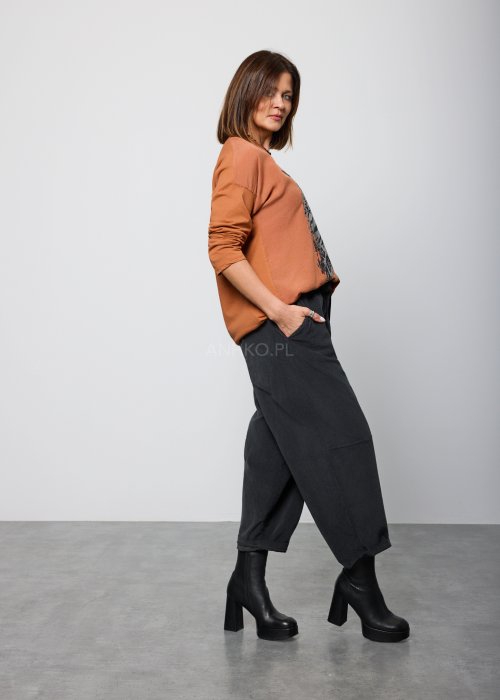 Modelka w brązowej bluzie z długim rękawem i ozdobnym nadrukiem w odcieniach złota i czerni