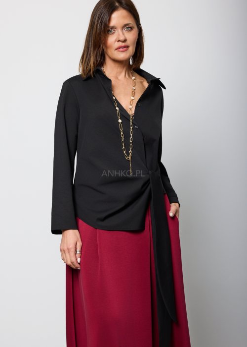 Czarna bluzka damska z asymetrycznym wiązaniem i klasycznym kołnierzem, o eleganckim fasonie. Stylizacja ze spódnicą w intensywnym kolorze w nowoczesnym wydaniu.