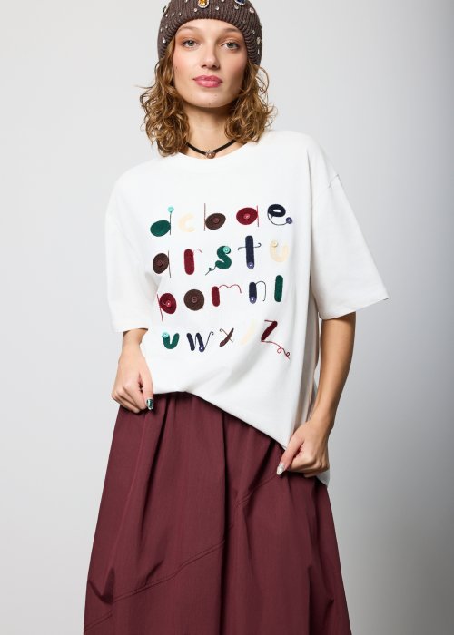 Biały damski T-shirt o luźnym kroju, z krótkim rękawem i okrągłym dekoltem, ozdobiony kolorowym haftem i aplikacjami w formie liter na przodzie; styl casual, artystyczny