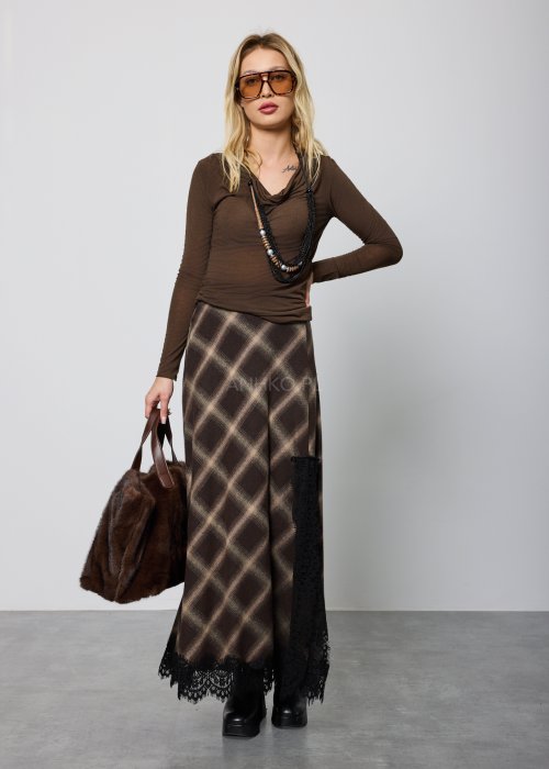 Długa damska spódnica w brązową kratę, o prostym, lekko rozszerzanym kroju; wykończona u dołu czarną koronką, noszona z czarnymi botkami na platformie.