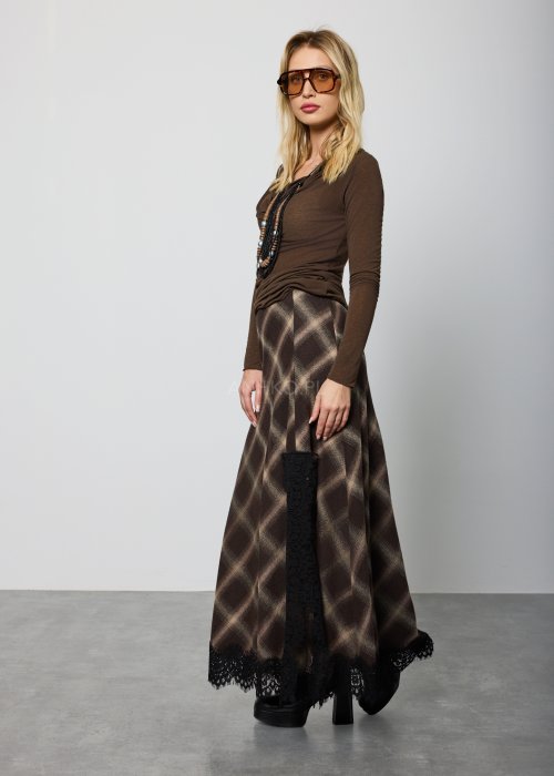 Długa damska spódnica w brązową kratę, o prostym, lekko rozszerzanym kroju; wykończona u dołu czarną koronką, noszona z czarnymi botkami na platformie.