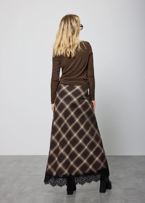 Długa damska spódnica w brązową kratę, o prostym, lekko rozszerzanym kroju; wykończona u dołu czarną koronką, noszona z czarnymi botkami na platformie.