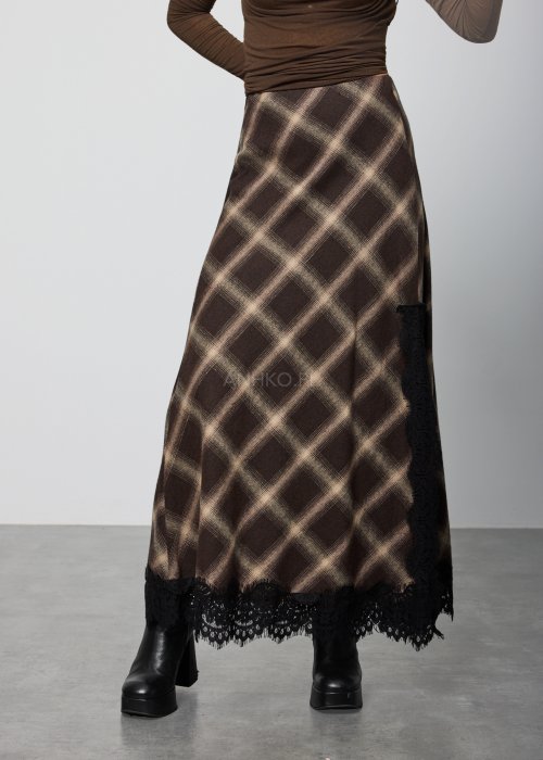 Długa damska spódnica w brązową kratę, o prostym, lekko rozszerzanym kroju; wykończona u dołu czarną koronką, noszona z czarnymi botkami na platformie.