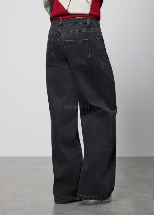 Czarne damskie jeansy z prostą, lekko rozszerzaną nogawką, klasyczny krój z pięcioma kieszeniami i zapięciem na guzik, noszone z białymi sneakersami.