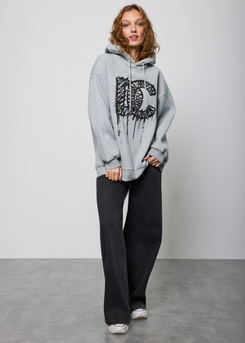 Damska szara bluza z kapturem o luźnym kroju, z dużym czarnym nadrukiem litery „C” ozdobionym aplikacjami i efektem spływającej farby