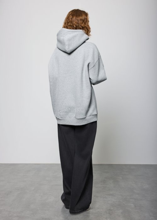 Damska szara bluza z kapturem o luźnym kroju, z dużym czarnym nadrukiem litery „C” ozdobionym aplikacjami i efektem spływającej farby