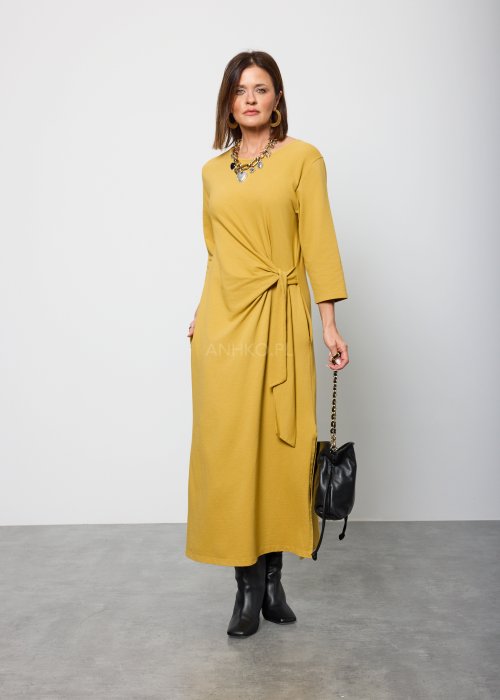 Damska sukienka midi w kolorze musztardowym, o prostym kroju z długimi rękawami i ozdobnym wiązaniem w talii po boku.