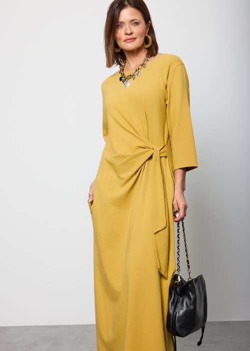 Damska sukienka midi w kolorze musztardowym, o prostym kroju z długimi rękawami i ozdobnym wiązaniem w talii po boku.