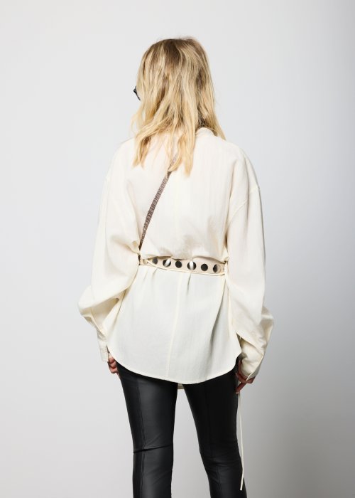 Kremowa damska bluzka o luźnym kroju, z długimi rękawami i miękko drapowanym dekoltem, przewiązywana cienkim paskiem w talii