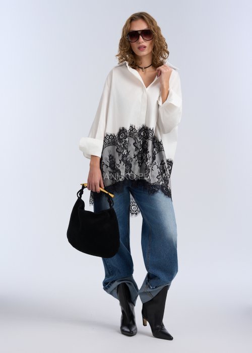 Biała koszula oversize z czarną, dekoracyjną koronką u dołu, długi rękaw i klasyczne zapięcie na guziki, stylizacja z jeansami.