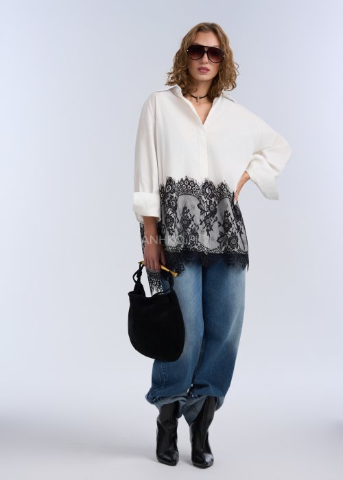 Biała koszula oversize z czarną, dekoracyjną koronką u dołu, długi rękaw i klasyczne zapięcie na guziki, stylizacja z jeansami.