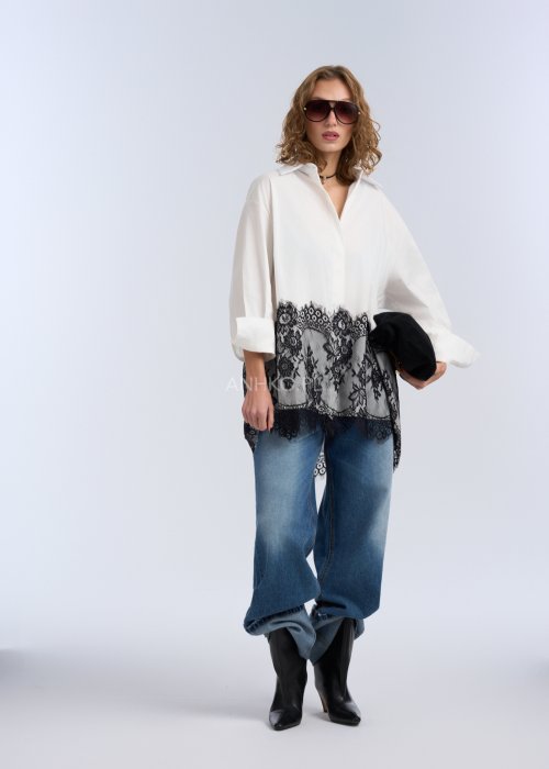 Biała koszula oversize z czarną, dekoracyjną koronką u dołu, długi rękaw i klasyczne zapięcie na guziki, stylizacja z jeansami.