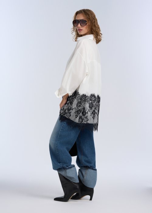 Biała koszula oversize z czarną, dekoracyjną koronką u dołu, długi rękaw i klasyczne zapięcie na guziki, stylizacja z jeansami.
