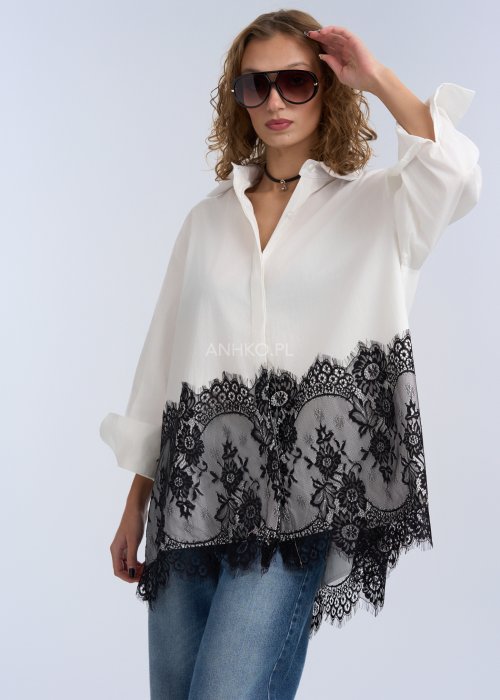 Biała koszula oversize z czarną, dekoracyjną koronką u dołu, długi rękaw i klasyczne zapięcie na guziki, stylizacja z jeansami.