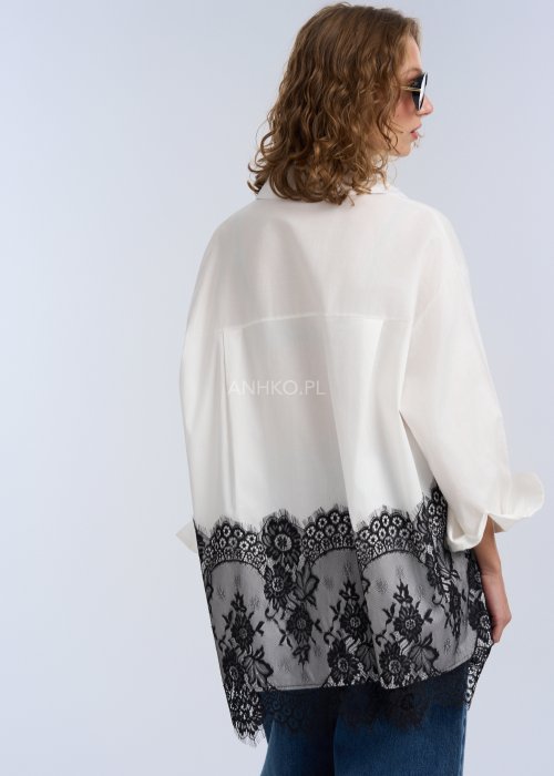 Biała koszula oversize z czarną, dekoracyjną koronką u dołu, długi rękaw i klasyczne zapięcie na guziki, stylizacja z jeansami.