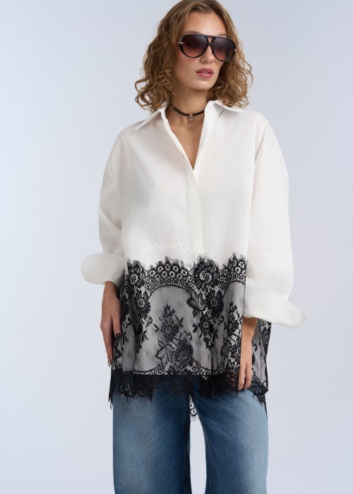 Biała koszula oversize z czarną, dekoracyjną koronką u dołu, długi rękaw i klasyczne zapięcie na guziki, stylizacja z jeansami.