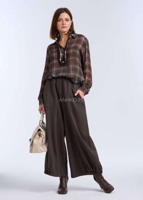 luźne, szerokie spodnie o długości do kostek, utrzymane w ciemnym, czekoladowo-brązowym kolorze. Mają elastyczną talię, która zapewnia wygodę i miękkie dopasowanie w pasie.