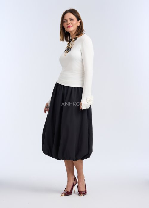 To dopasowana, jasna (kremowo-biała) bluzka z długim rękawem, wykonana z gładkiej, elastycznej dzianiny