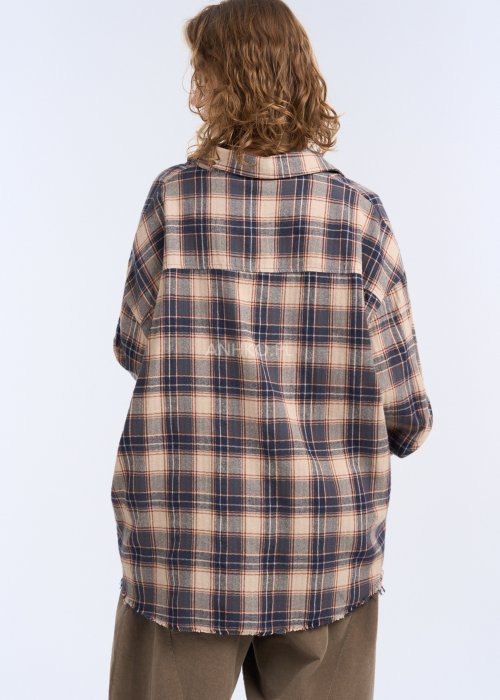 To luźna koszula w kratę w stonowanej kolorystyce beżu, granatu i ciepłego brązu. Ma oversize’owy fason, długie rękawy z mankietami oraz klasyczne zapięcie na guziki