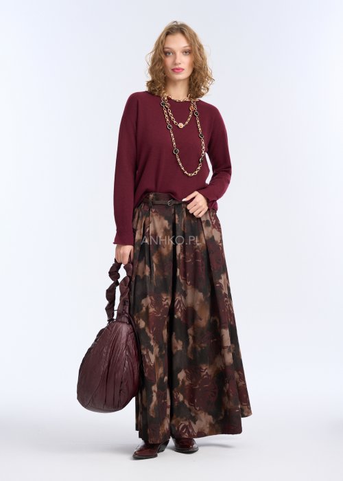 Modelka w bordowej, gładkiej bluzce z długim rękawem i prostym dekoltem; luźny fason, miękka dzianina, bluzka zestawiona z długim naszyjnikiem w kolorze złota