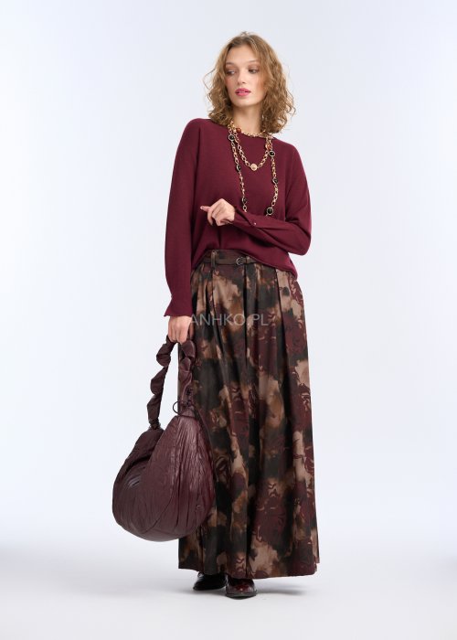 Modelka w bordowej, gładkiej bluzce z długim rękawem i prostym dekoltem; luźny fason, miękka dzianina, bluzka zestawiona z długim naszyjnikiem w kolorze złota